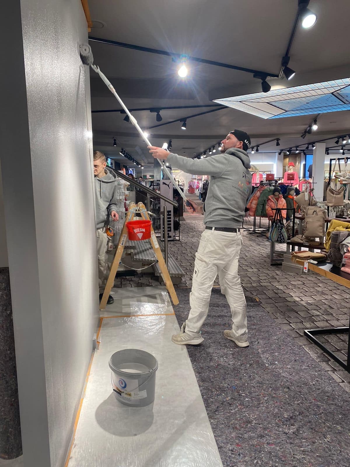 Maler rollt eine graue Wand in einem Ladenlokal