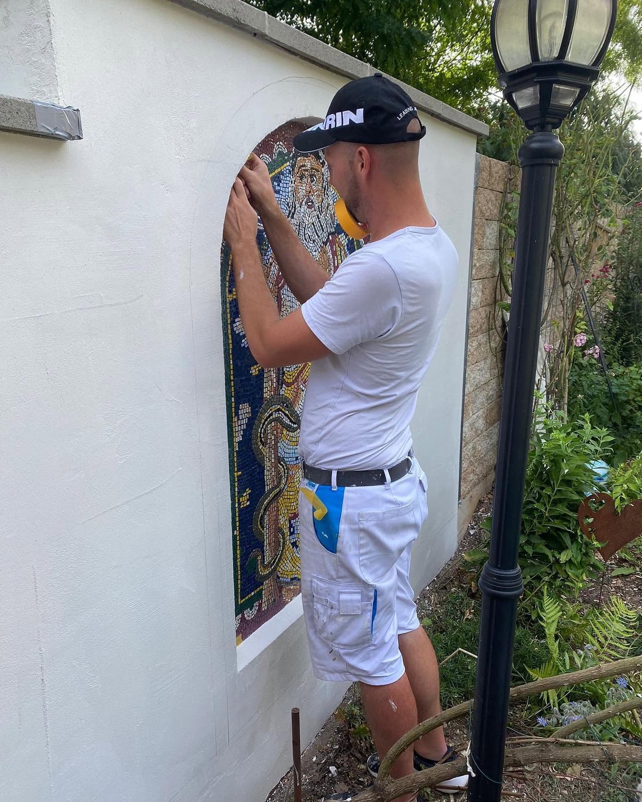 Handwerker bringt ein Mosaik an einer Gartenmauer an