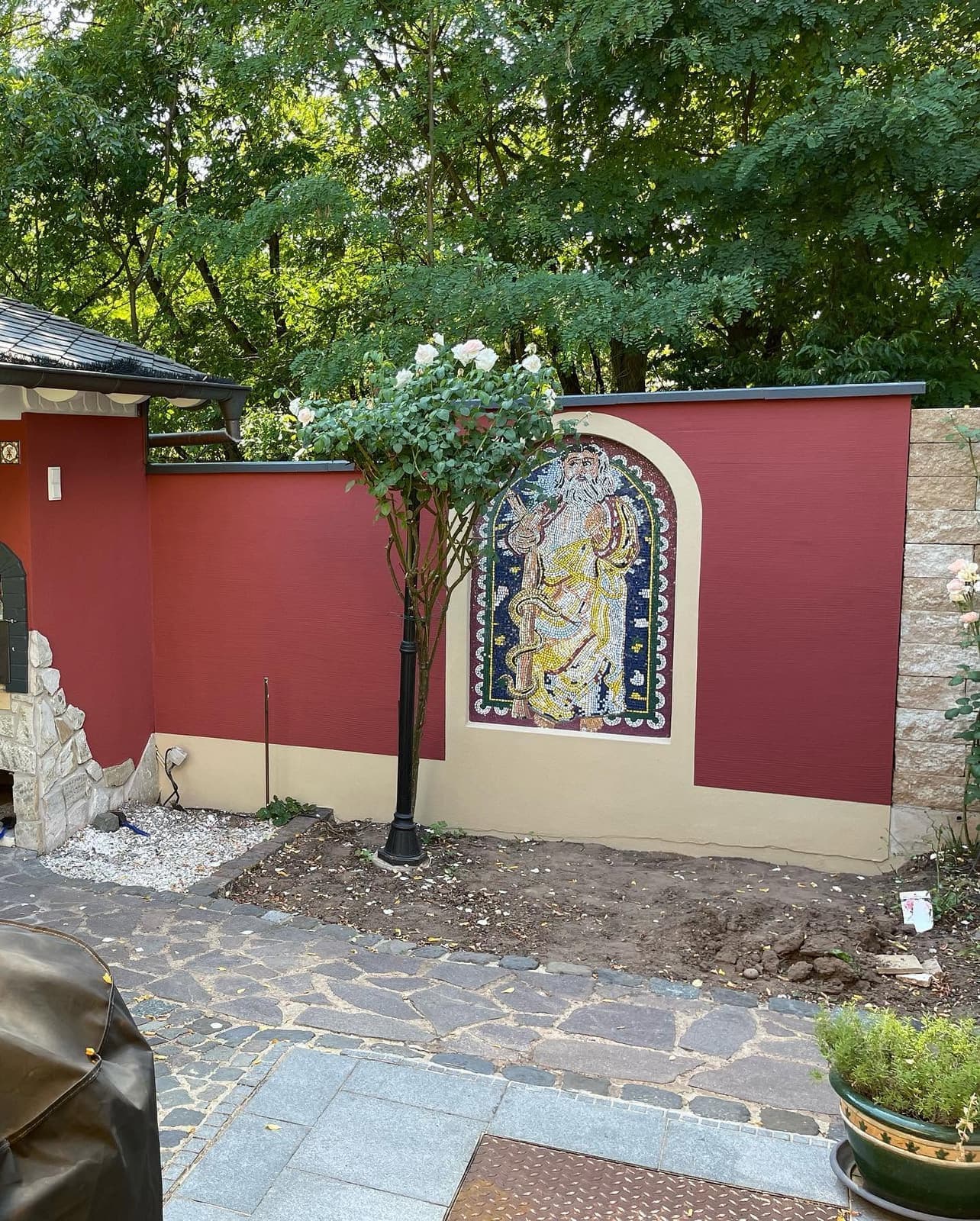 Rot gestrichene Gartenmauer mit Mosaik im Garten