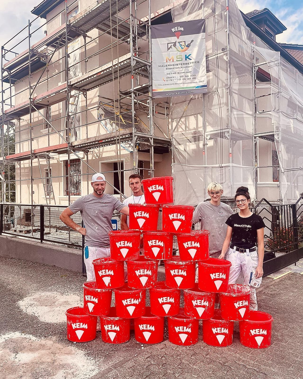 Das M|S|K Team vor einem eingerüsteten Haus mit Farbeimern