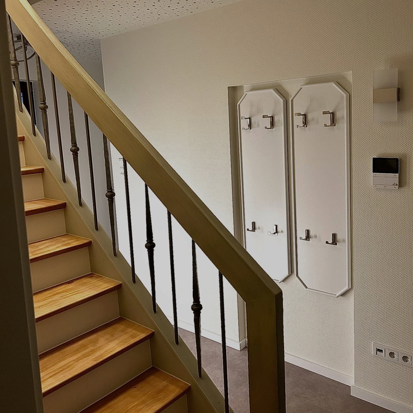Renovierter Flur mit heller Holztreppe, weißen Wänden und Garderobe